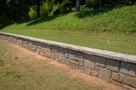 Low granite block retaining wall in an urban park, green grass and trees, horizontal aspectの写真素材