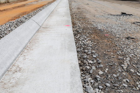 View straight down a section of extruded concrete curb, street construction detail with gravel and dirt, horizontal aspectの写真素材