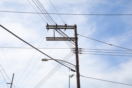 Wood electrical power pole with lines running in multiple directions, street lights and blue sky,...