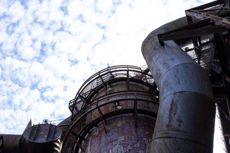 Tubes and blast furnace structure with circular grate catwalks, blue sky with clouds copy space,...