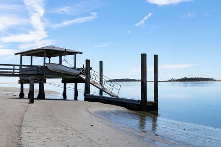 Private boat dock on Tybee Creek at the Atlantic Ocean, sandy beach and still blue waters beneath a bright blue sky with clouds, Tybee Island Georgia, horizontal aspectの写真素材