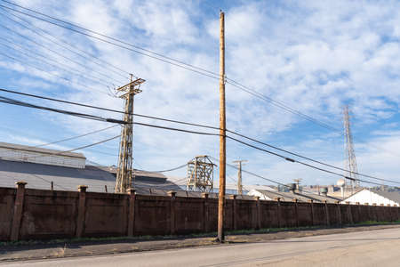 Long wall between street and industrial steel mill, power lines, blue sky with clouds, horizontal aspectの写真素材
