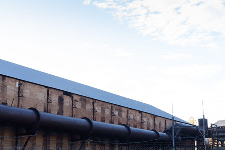 Very large tube running along the outside of a large industrial building in early morning, light...