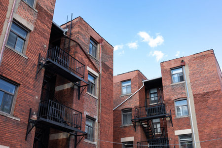 Urban landscape rear view of old brick apartment buildings with black metal fire escapes against a bright blue sky, horizontal aspectの写真素材