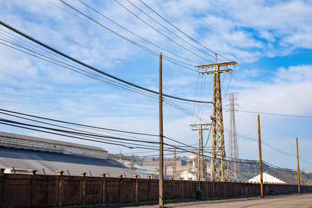 Tall metal power towers and wood power poles carry lines through a large industrial facility under...