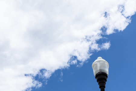 Exterior light post with glass fixture isolated against a blue sky with white clouds, creative copy space, horizontal aspectの写真素材