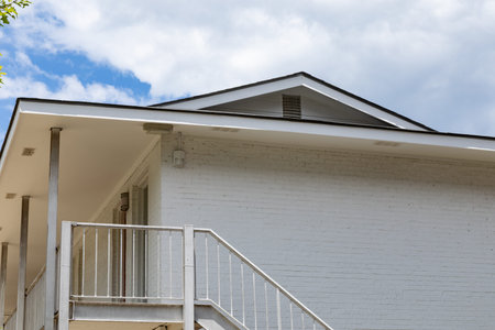 Generic brick apartment building painted white, second floor with metal railing and stairs, blue sky...