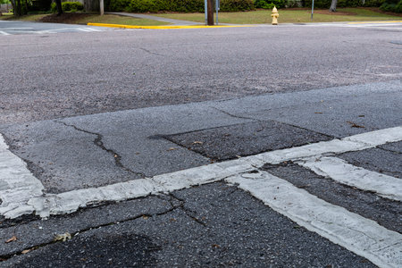 Wide view of an intersection of two streets with painted crosswalks, cracked and weathered road...