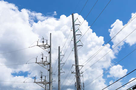 Elaborate metal power poles with stacks of electrical lines against a brilliant blue sky with bright white clouds, horizontal aspectの写真素材