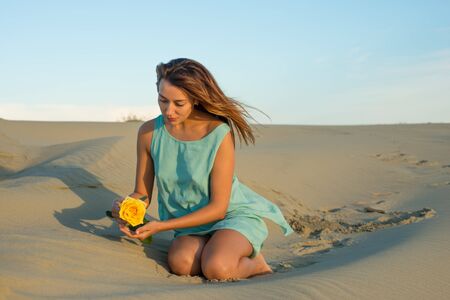 Woman with a yellow rose sits on the sandの写真素材