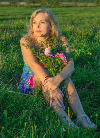 Woman sitting on the grass with flowersの写真素材