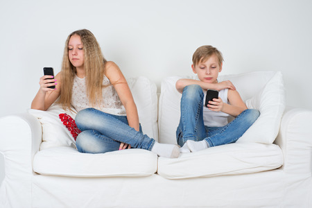Boy and girl sitting on the couch with your phoneの写真素材