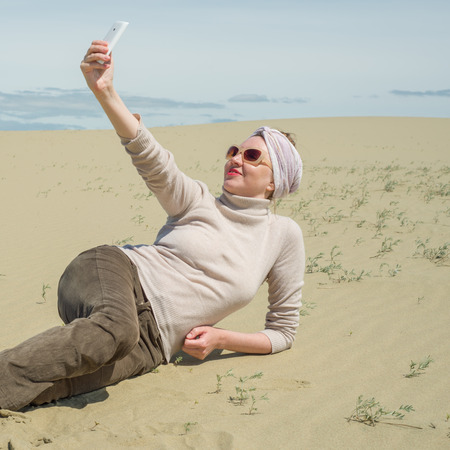Woman lying on sand and looking at the smartphoneの写真素材