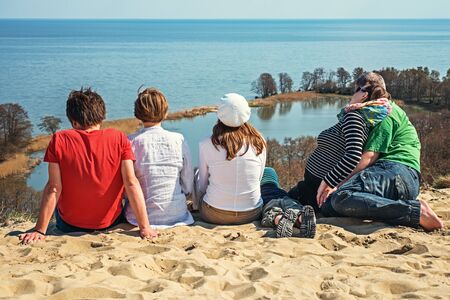 Young people sitting on a sandy hill and look at the bayの写真素材