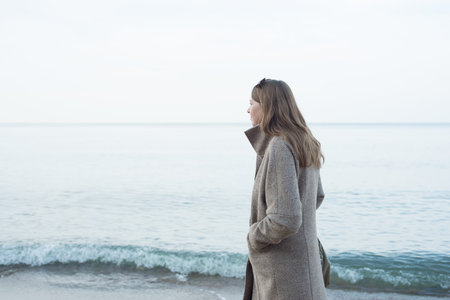 Woman walks in a gray coat near the seaの写真素材