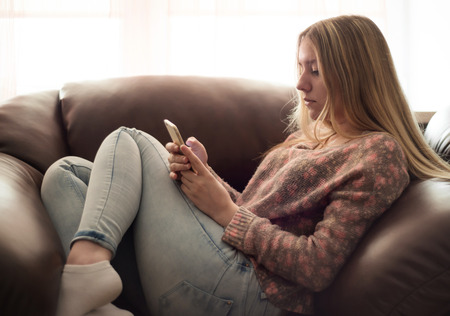 Teenage girl sitting in a chair and enjoys a smartphoneの写真素材