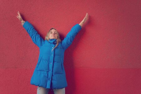 Girl teenager standing near a red surface with hands raisedの写真素材