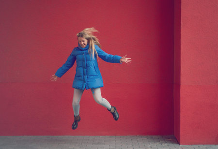 Teenage girl is jumping against a red wall