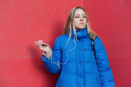 Girl teenager standing near a red wall uses a smartphoneの写真素材