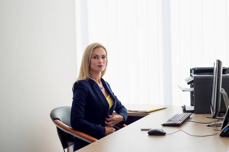 Business woman sitting at the table and buttoning up the jacketの写真素材