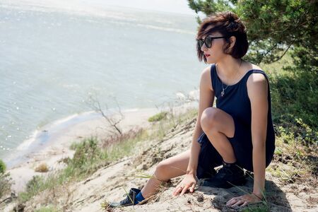 Young woman in a dress sits on the edge of a cliffの写真素材