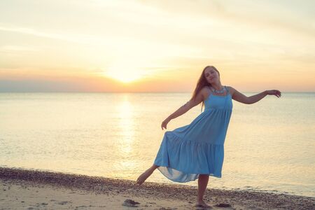 Woman with long hair in a dress dancing near the seaの写真素材