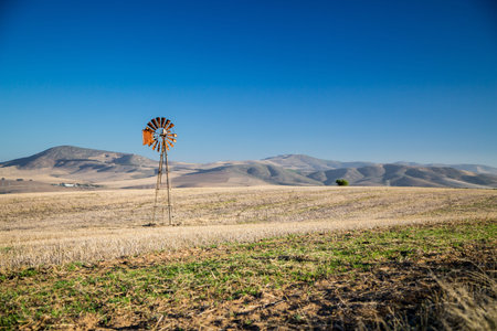 A wind pump in the middle of dry fields with hills in the background の写真素材