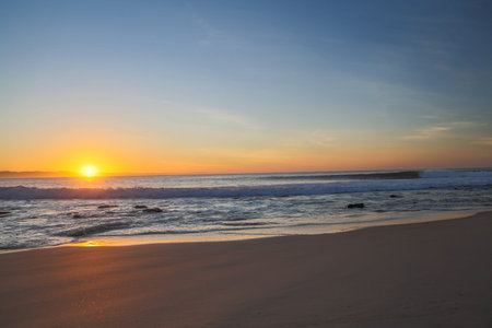 A right hand wave breaking in the sea as the sun rises for the start of a new dayの写真素材