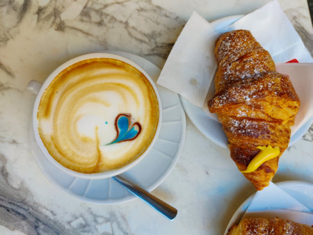A cup of cappuccino and croissant on the tableの写真素材