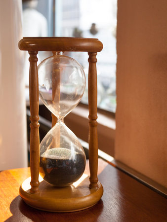 Sandglass, hourglass on table near window.
