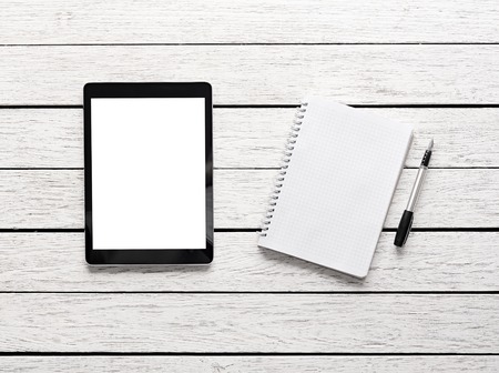 Tablet computer with notepad on white wooden desk. Clipping path included.の写真素材