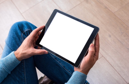 Man using tablet computer while sitting on a wooden floor. View from above. Clipping path included.の写真素材