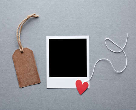 Instant photo frame with blank gift tag and small red heart. On gray paper background.の写真素材