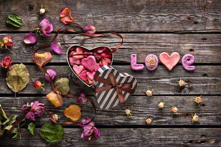 Word Love with heart shaped Valentines Day gift box on old vintage wooden plates. Sweet holiday background with rose petals and dried rose flowers.の写真素材
