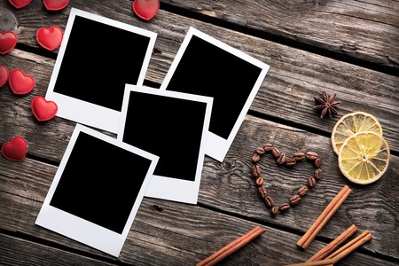 Four blank instant photo frames with small heart shapes and cinnamon on old wooden backgroundの写真素材