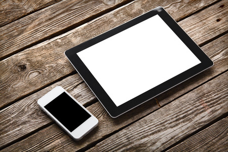 Digital tablet computer and white smart phone with isolated screens on old wooden desk.の写真素材
