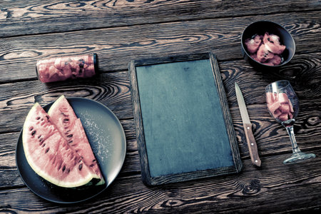 Mockup of a chalkboard on dark desktop with sliced watermelon. Top view.の写真素材