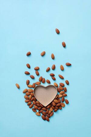 Open and empty heart shaped box among scattered from it to the top almond. Top view background.の写真素材