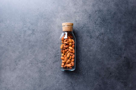 Almond nuts in corked glass jar on a concrete desktopの写真素材