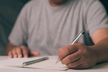 Man hand is writing on notebook with pen on desk officeの写真素材