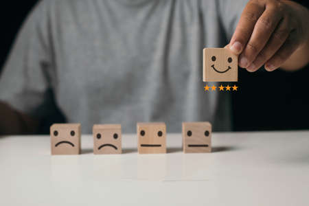 Close up man hand choose smiley face icon on wood cube, customer Service rating, evaluation and satisfaction survey concept.の写真素材
