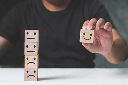 Close up man hand choose smiley face icon on wood cube, customer Service rating, evaluation and satisfaction survey concept.の写真素材