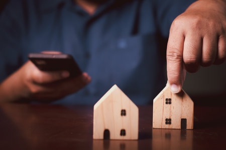 Man hand holding wood house model with using smartphone to Planning buy Real Estate, Planning to buy property investment and house mortgage financial concept.の写真素材