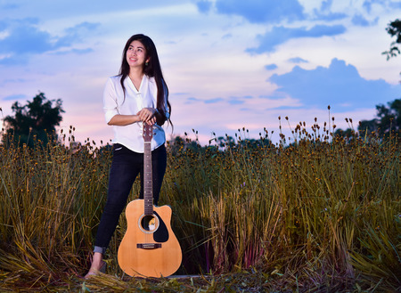 Asian girl standing embracing a guitar in a field of flowers. Feel the love of music.
