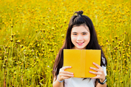 Lovely Asian girl holding yellow book. Standing smile in the middle of a yellow flower garden. The Concept of Love, Reading and Educationの写真素材