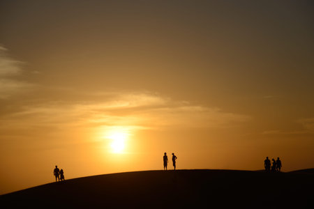 Group of people on top of large sand dune on horizon watching the setting sun の写真素材
