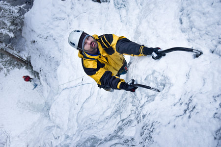 Man climbs up a frozen waterfall with ice ax.