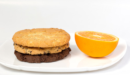 slice of orange and three cookies on a white plateの写真素材
