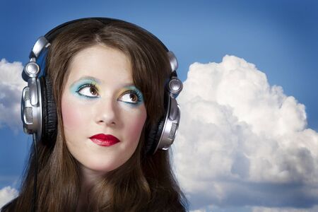 Beautiful Girl listening music over clouds backgroundの写真素材