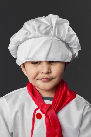 Pretty little boy preparing healthy food on kitchen over grey background, cook hatの写真素材